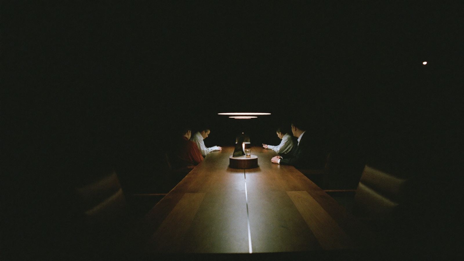 Cuatro personas conversando en una mesa larga, bajo una luz lineal